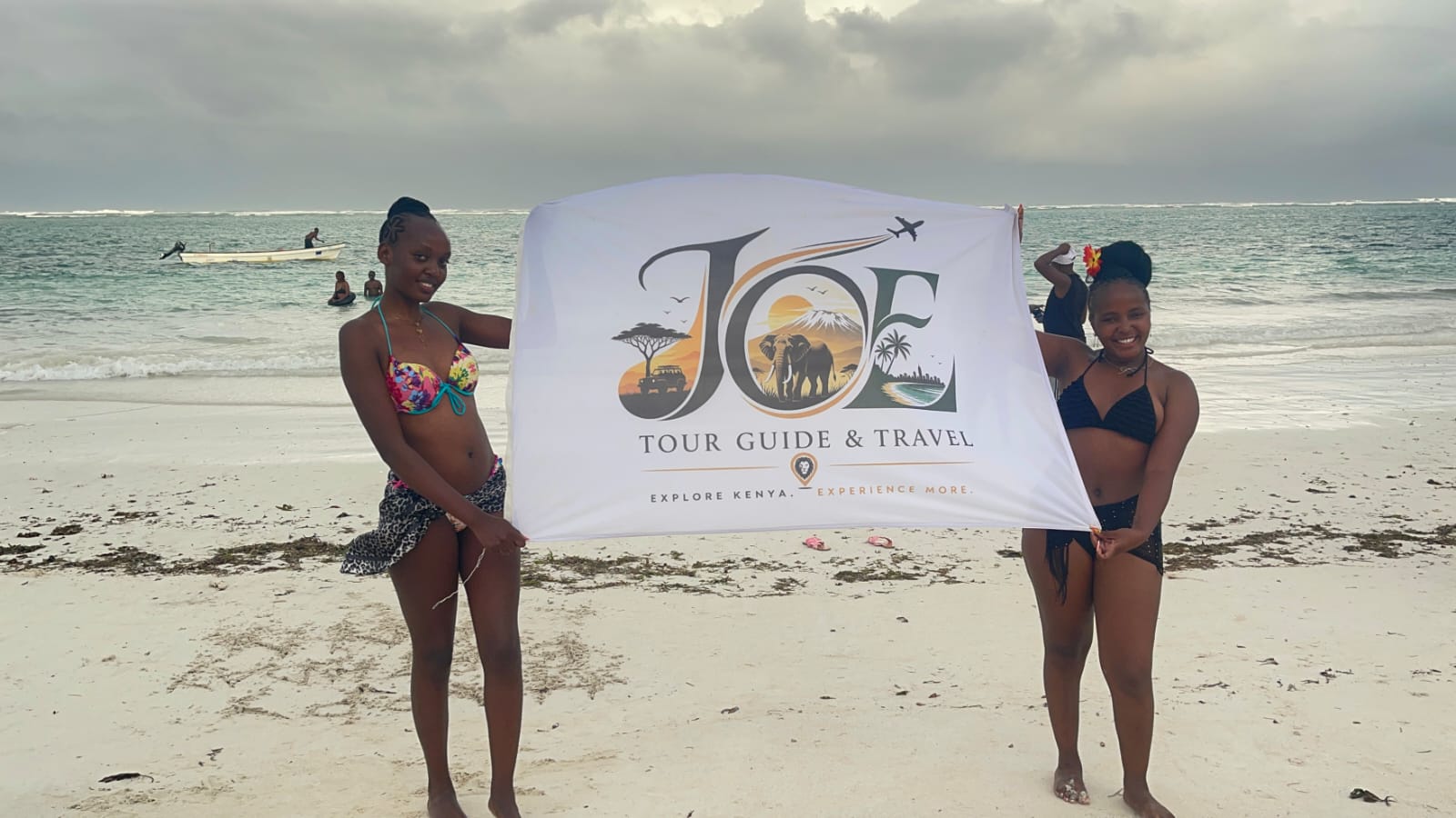 Guests holding the JOE Tour Guide & Travel flag by the Indian Ocean