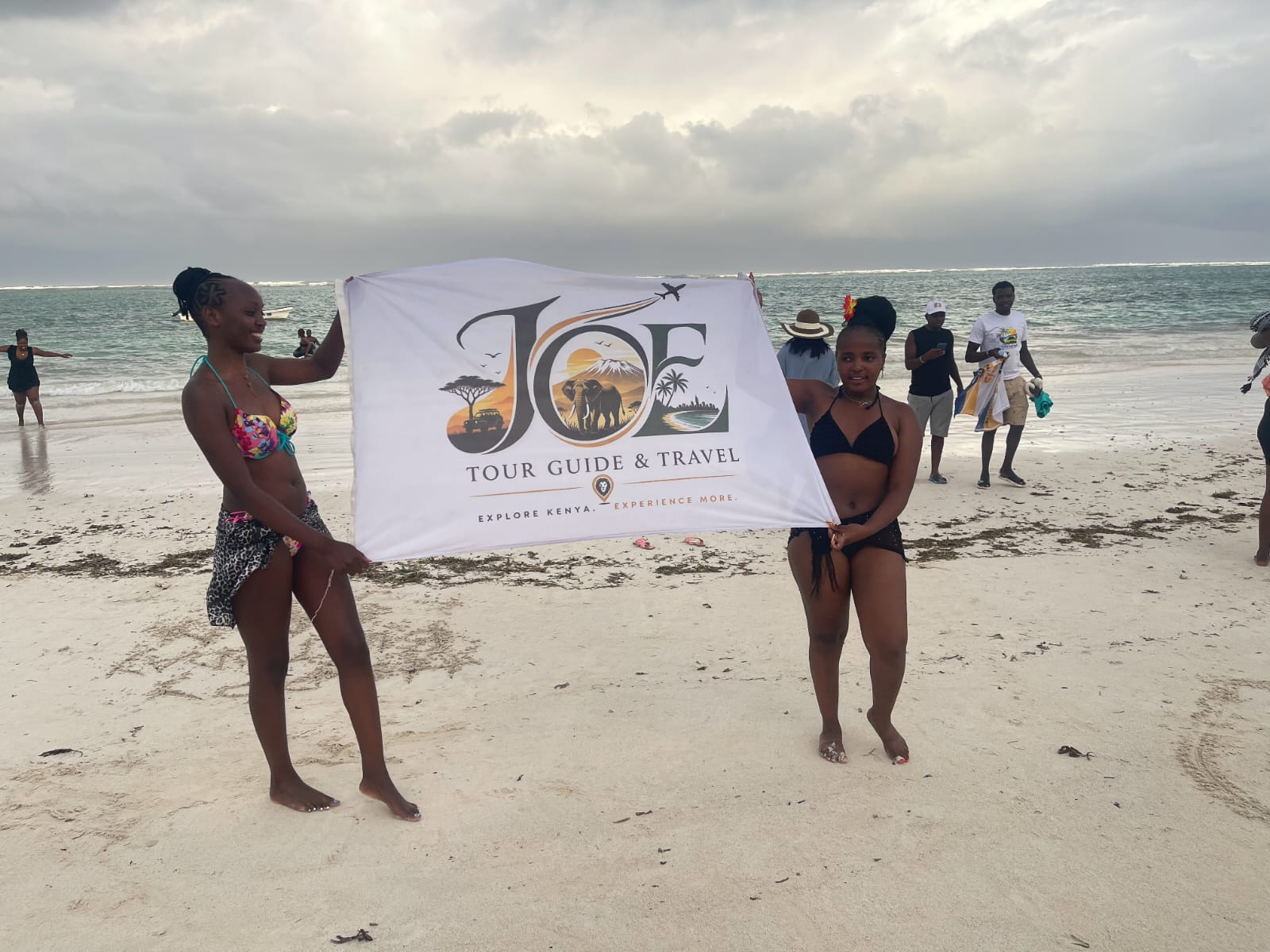 Guests posing with the JOE Tour Guide & Travel flag on the beach