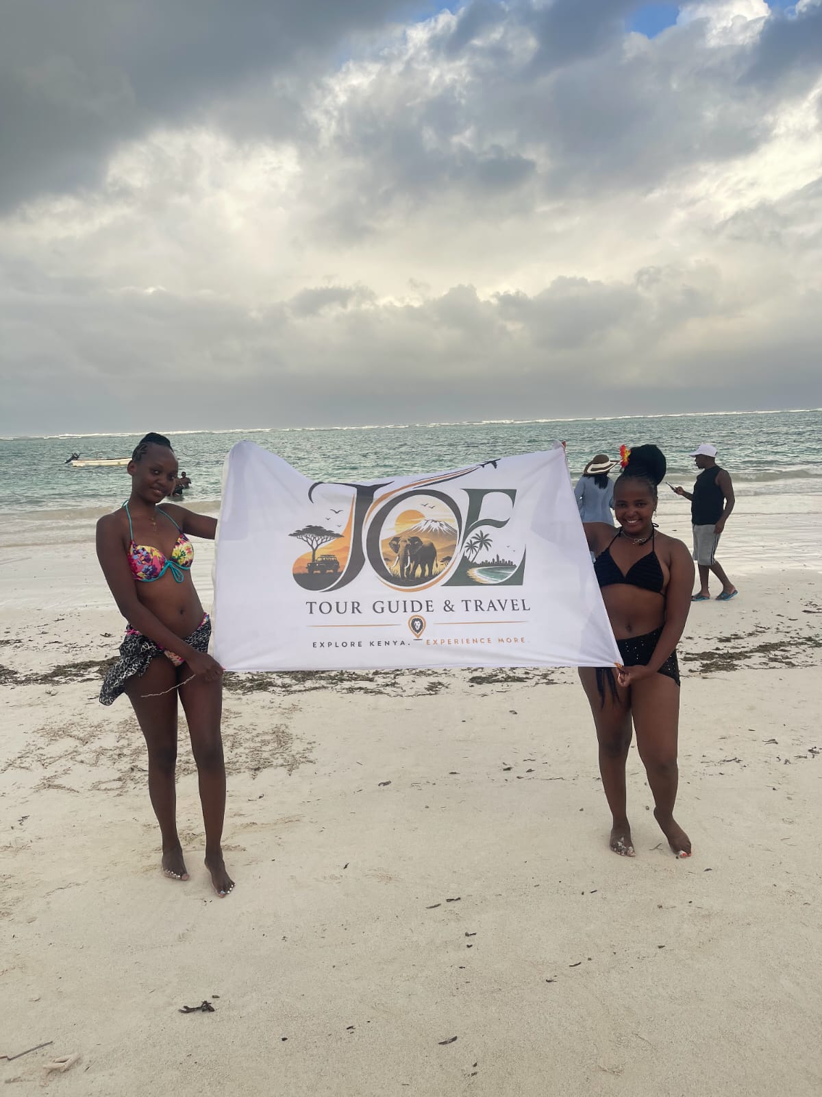 Guests holding the JOE Tour Guide & Travel flag with the ocean behind them
