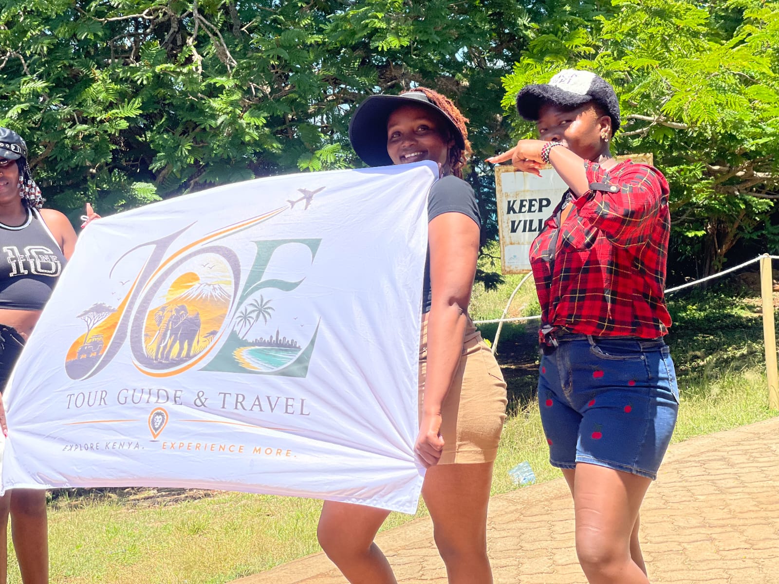 Guests holding the JOE flag near the Kenya Wildlife Service village sign