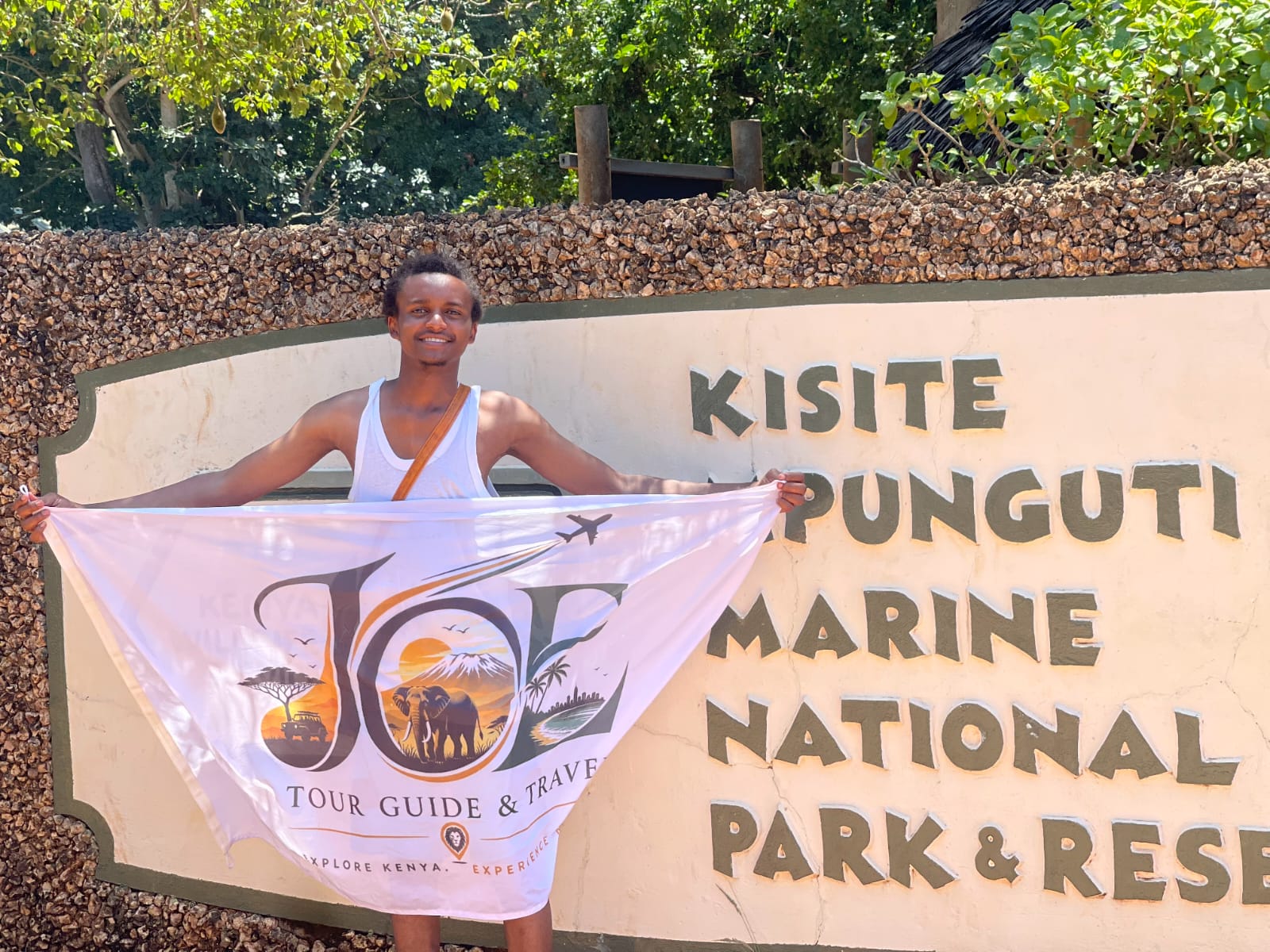 Guest holding the JOE flag at the Kisite-Mpunguti Marine National Park sign