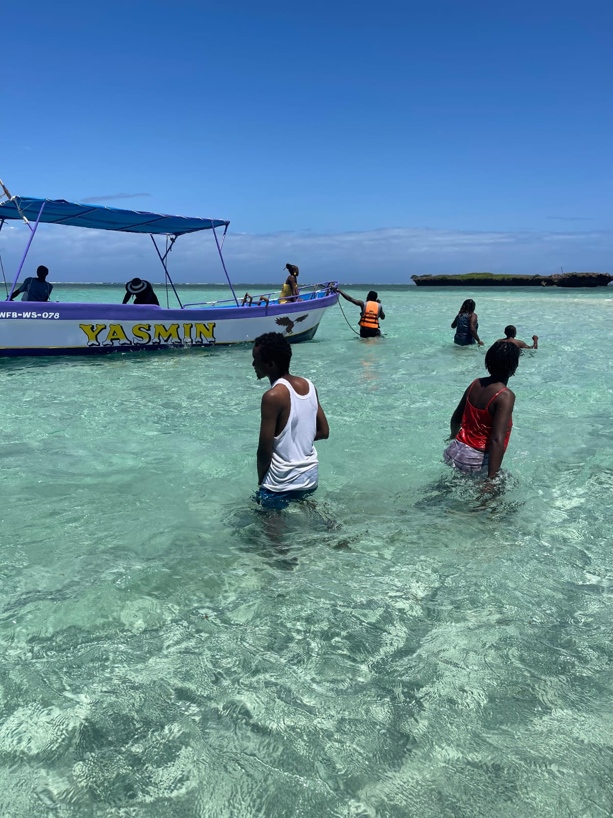 Guests wading through clear turquoise water beside the Yasmin boat